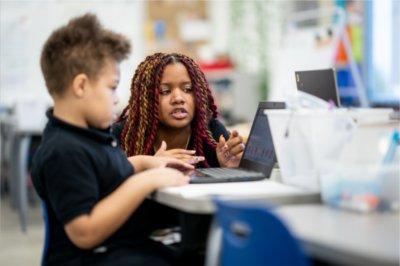 老师跪在一个正在看笔记本电脑的二年级学生的桌子旁